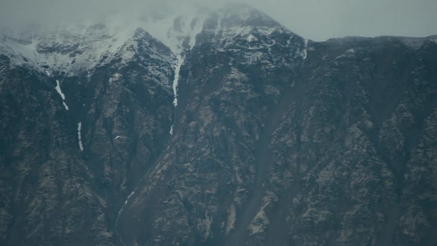 An adventurous paraglider drifts slowly across a vast, snowcapped mountain range shrouded in mist