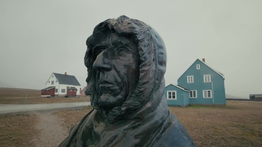 A close-up of a weathered bronze statue of a polar explorer in a remote village on a foggy day