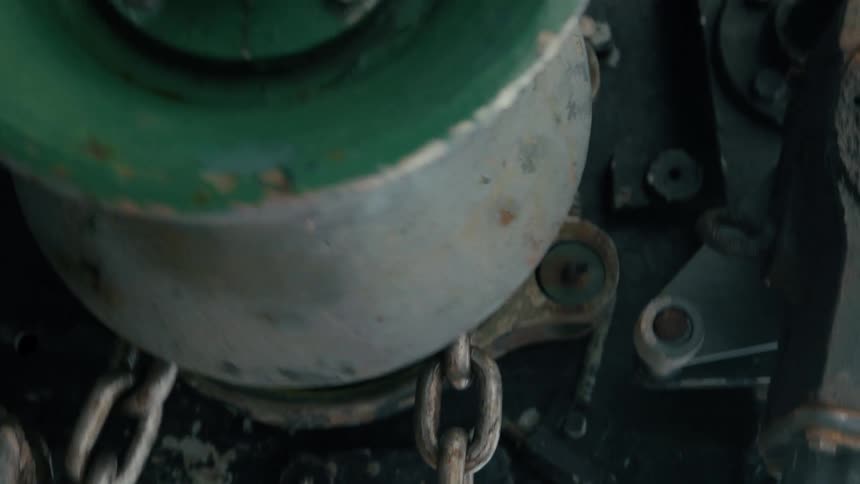 A close-up vertical shot of an old, rusty industrial chain and green painted machinery in a workshop