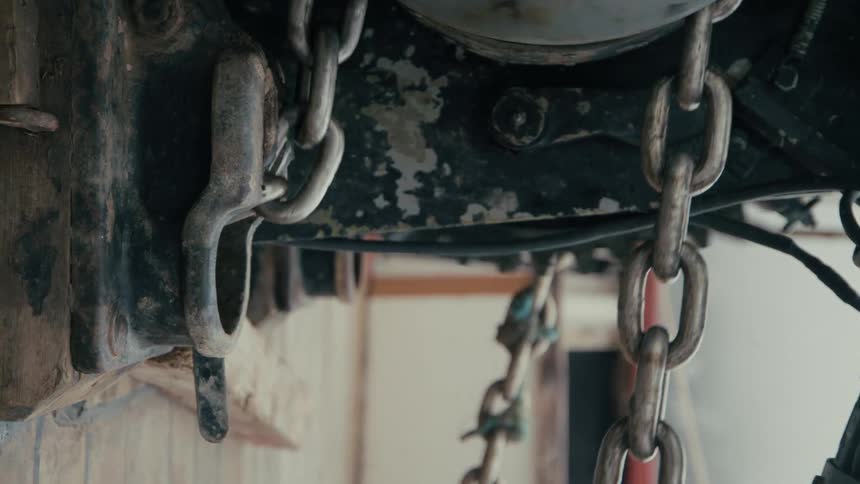 A close-up vertical shot of weathered industrial chains hanging from heavy machinery and swaying gently