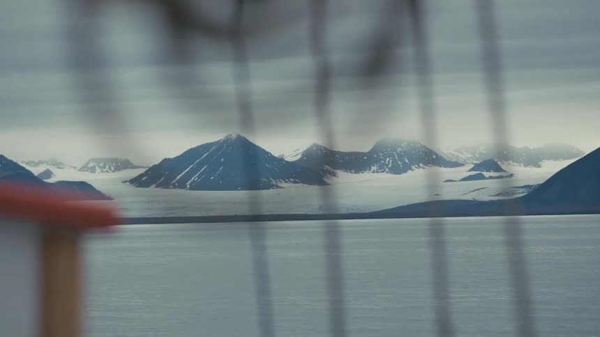 A serene, slow pan reveals a vast arctic landscape of snow-covered mountains and a frozen sea, viewed from a boat