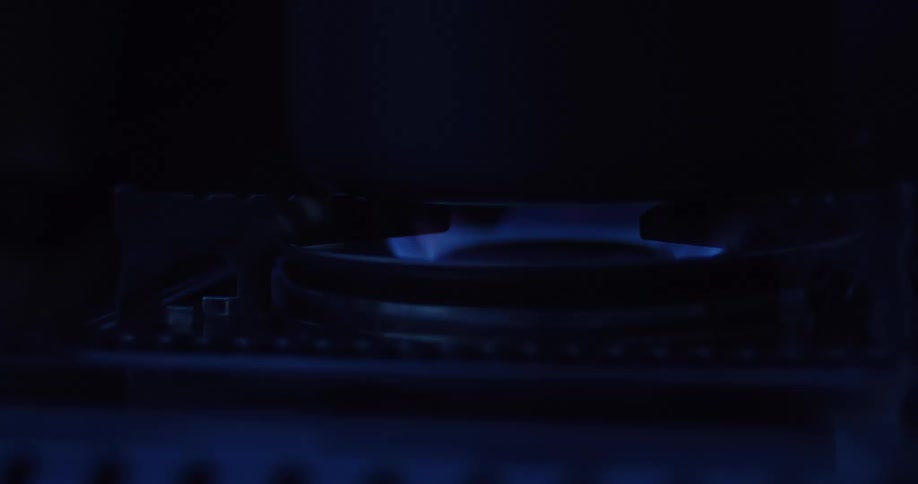 A close-up shot of a blue gas flame burning on a stove top burner in the dark