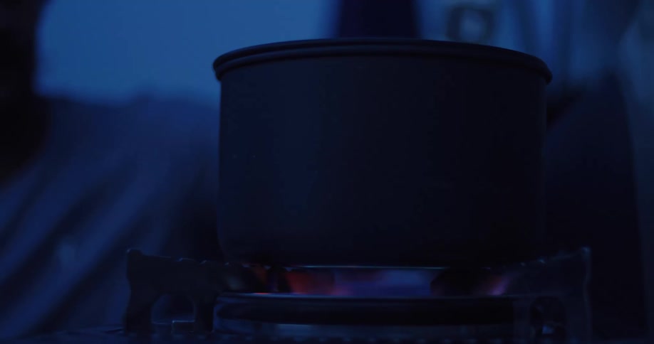 A close-up shot of a black camping pot heating up on a portable stove in the dark
