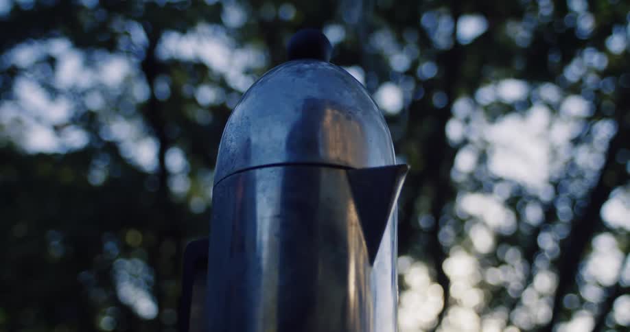 Steam gently rises from a Moka coffee pot brewing outdoors amongst the trees