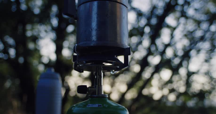 Close-up of a portable camping stove igniting to brew coffee in the woods at dusk