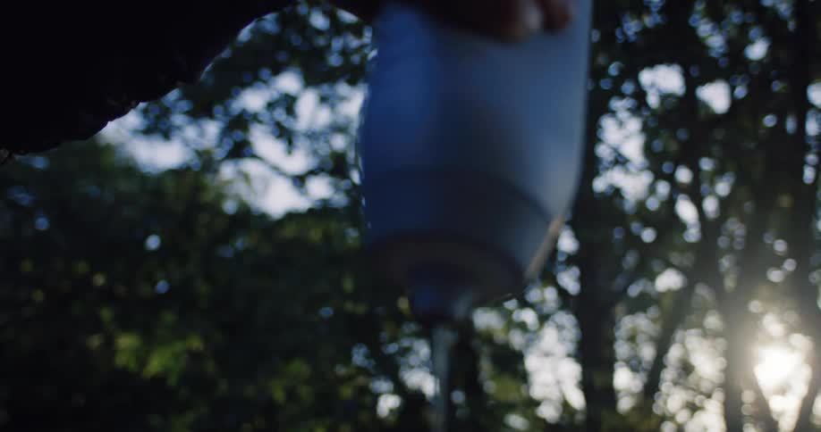 Slow motion shot of water being poured from a water filter into a moka pot for morning coffee at a sunny campsite