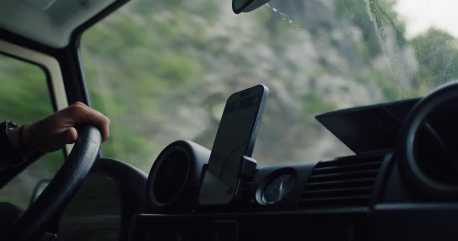 A smartphone with a GPS navigation app guides a driver out of a dark tunnel into the light of day on a road trip