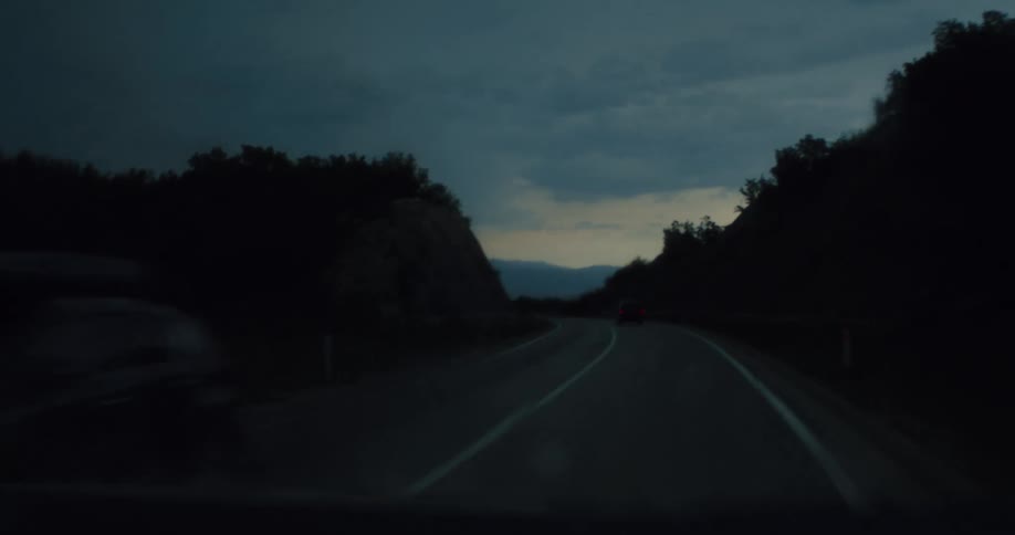 Point-of-view of driving a car on a winding country road on a rainy evening as wipers clear the wet windshield
