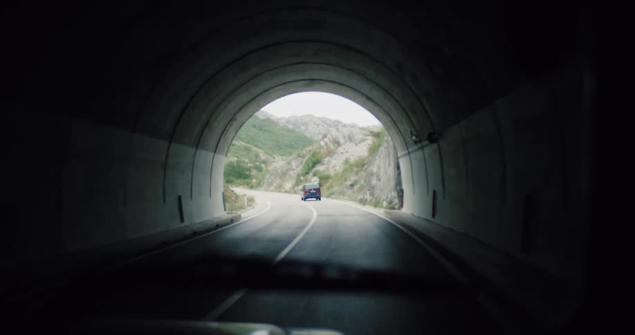 Point-of-view shot of a car exiting a dark tunnel and driving onto a winding mountain road