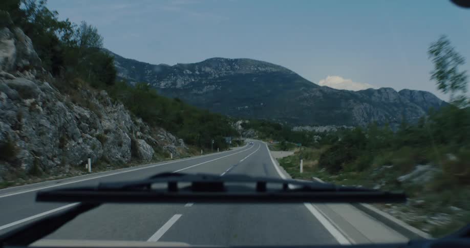 The view from a car's windshield reveals a winding journey through a rugged and beautiful mountain pass