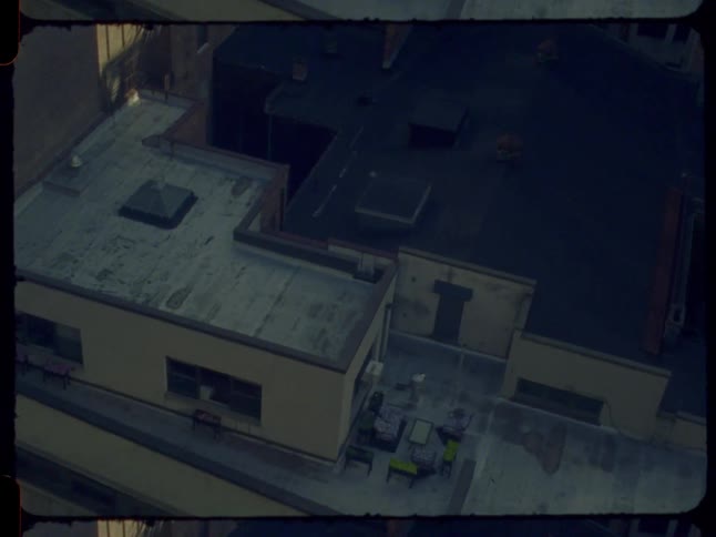 Vintage 16mm film captures a slow-moving, high-angle view of a dense city skyline and its rooftops