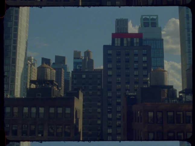 A vintage 16mm film timelapse captures the shifting afternoon light and shadows across the New York City skyline and iconic rooftop water towers