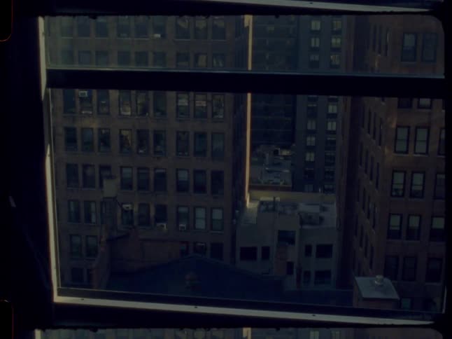A vintage film shot tilts up from a dark room window to reveal the classic brick buildings and water towers of the New York City skyline