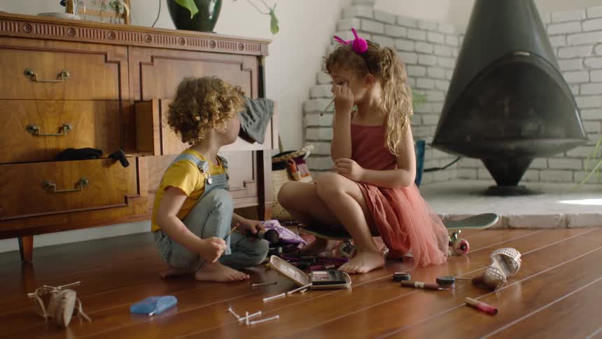 Adorable young siblings play together with their mother's makeup on the living room floor