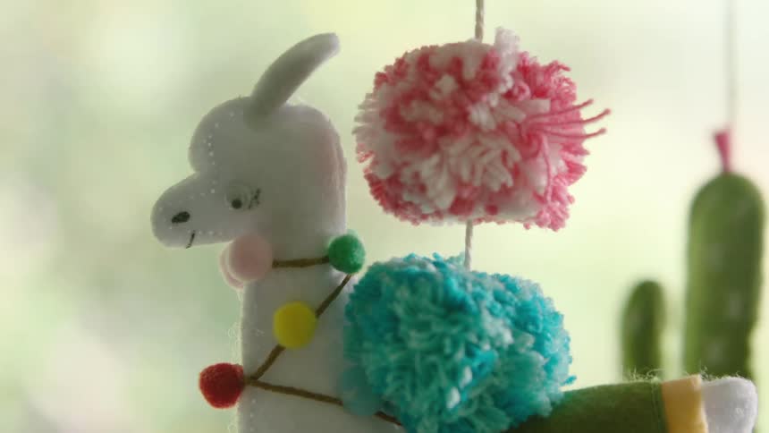 A close-up shot of a colorful, handmade felt llama baby mobile gently swaying in a nursery