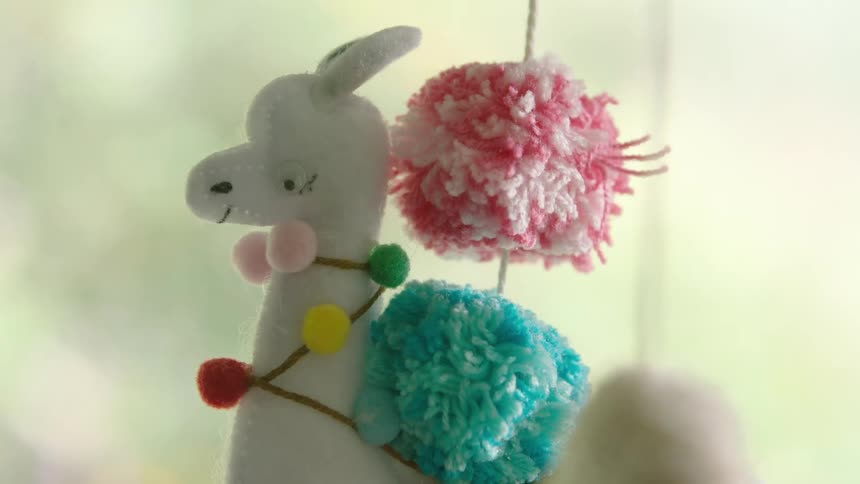 A cute handmade felt llama with colorful pom-poms on a baby mobile slowly comes into focus