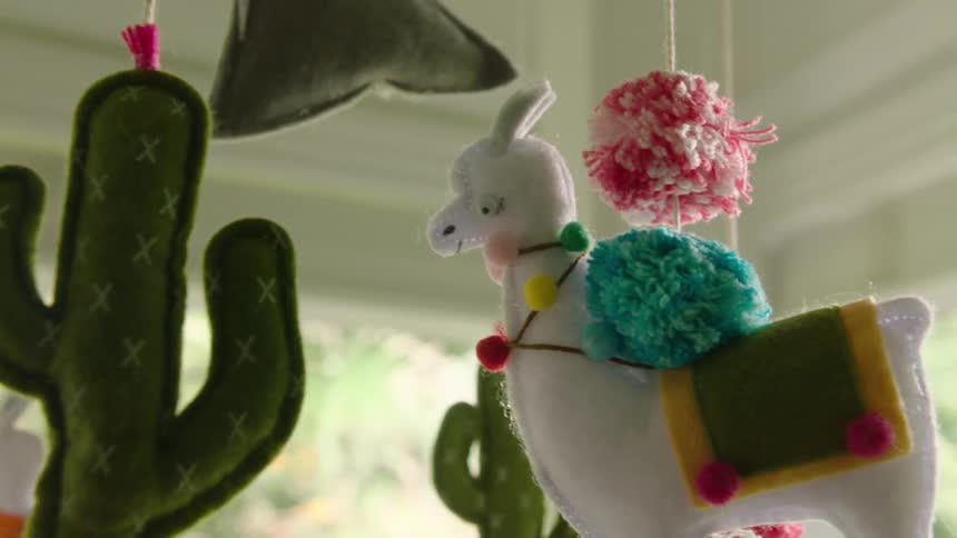 Colorful handmade felt baby mobile featuring a llama and cacti hangs in a nursery