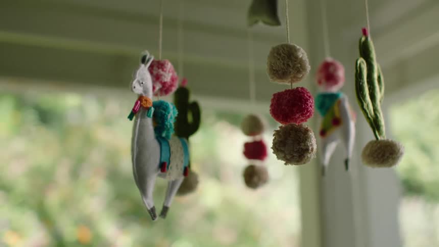 A handmade felt baby mobile featuring llamas and cacti gently sways in the soft light