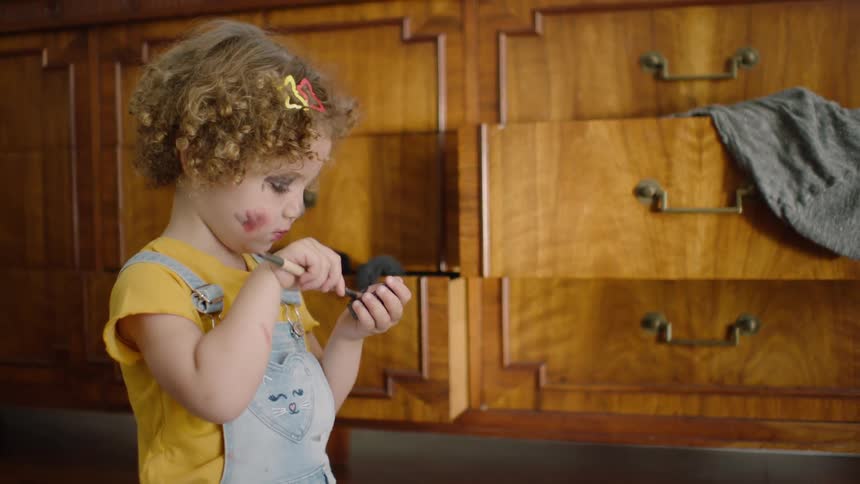 Slow motion shot of a funny little girl with makeup all over her face trying to apply more eyeshadow