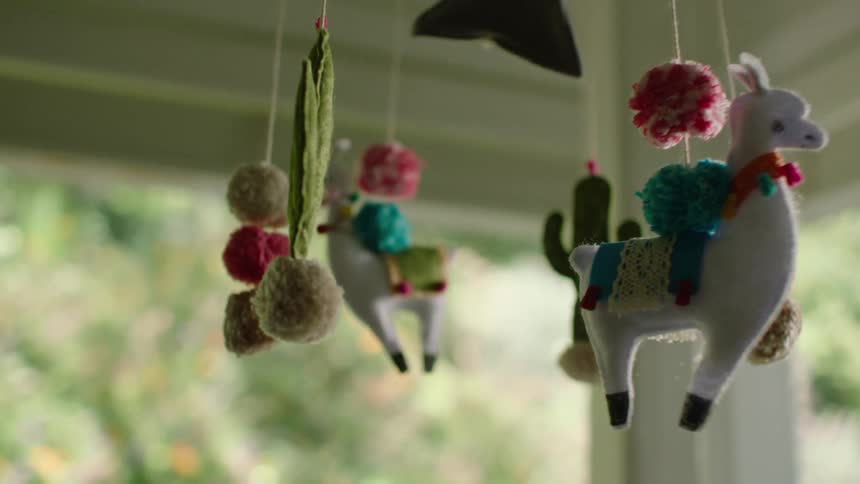 A handmade baby mobile with felt llamas and cacti slowly spins and comes into focus against a soft green background