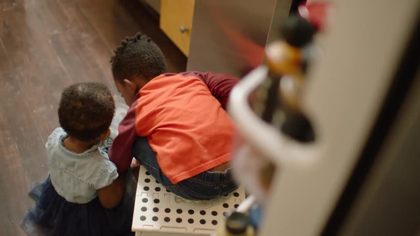 High angle shot of a young boy and his baby sister sitting on the kitchen floor with a container of blueberries
