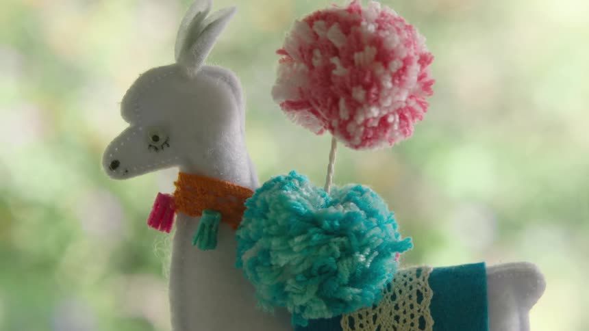 Close-up pan of a whimsical, handmade felt llama and cactus mobile hanging in a softly lit room