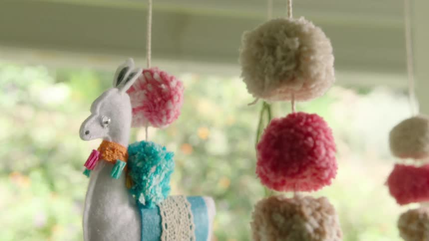 A charming, handmade felt llama and cactus baby mobile sways gently in front of a bright window