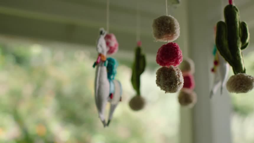 A handmade felt baby mobile with llamas, cacti, and colorful pom-poms gently spins in slow motion
