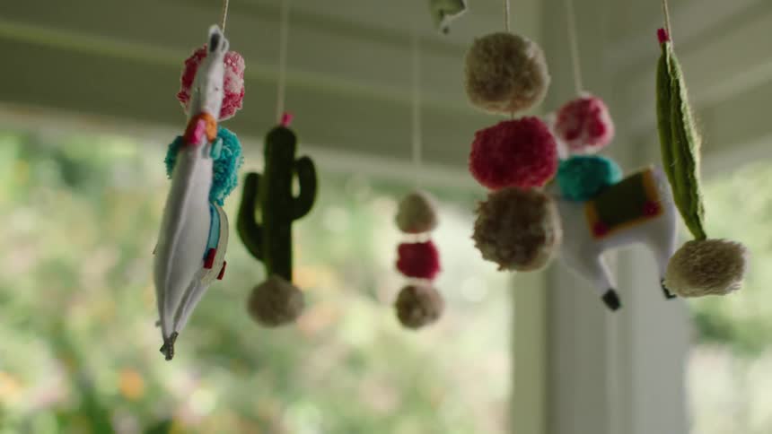 A whimsical felt llama and cactus baby mobile gently turns in slow motion with a shallow depth of field