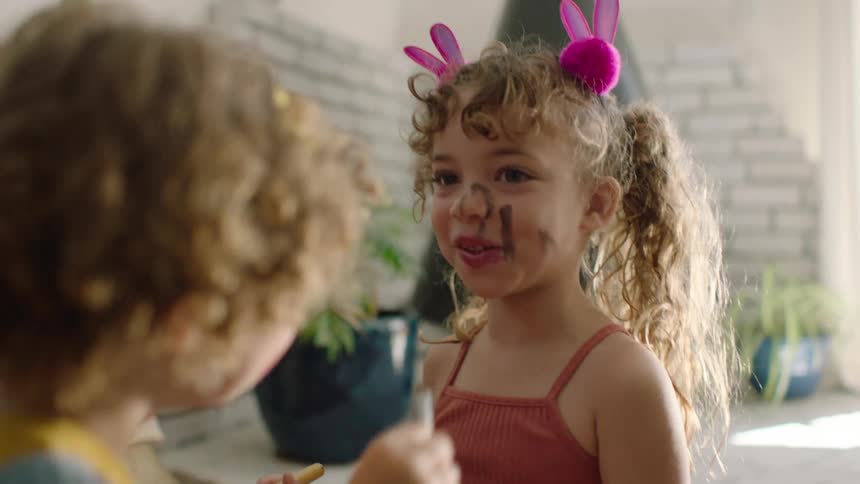 Adorable siblings with messy makeup faces laugh while playing dress-up together in their home
