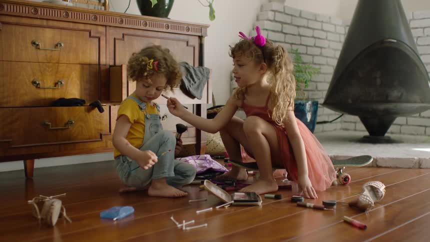 Slow reveal of two cute siblings playing with makeup on the floor, the older sister carefully applying it to the younger one's face