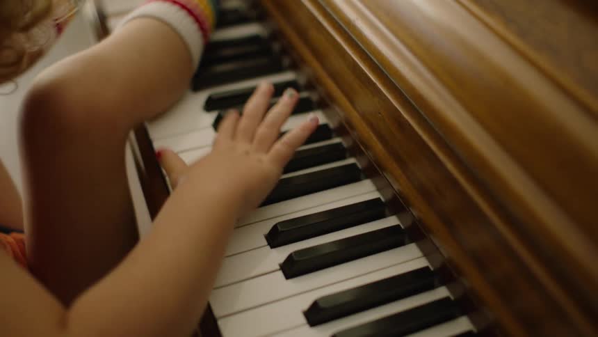 A curious toddler with rainbow socks and colorful nails playfully explores a piano with both hands and feet