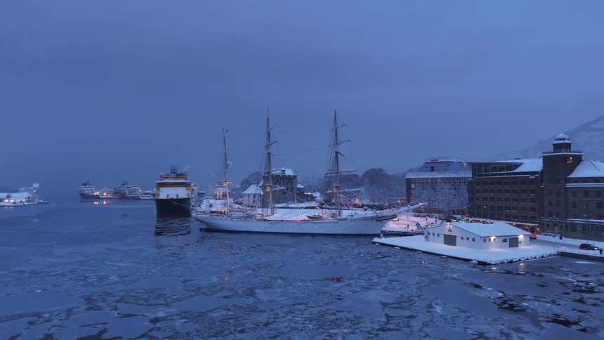 An aerial view reveals a majestic tall ship docked in a frozen, snow-covered harbor during a serene winter twilight