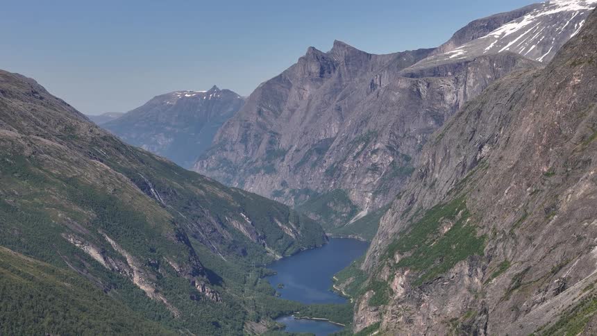 A breathtaking high-angle view of a serene lake nestled within a vast, rugged mountain valley with snow-capped peaks