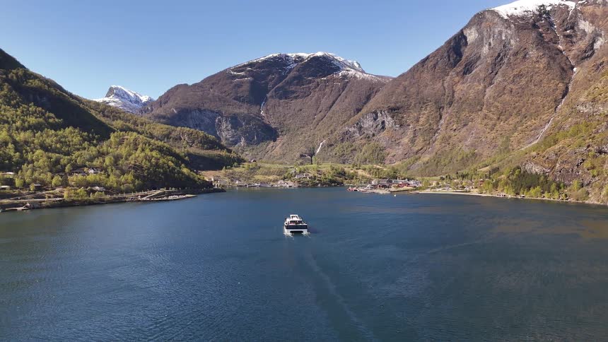 A majestic aerial view captures a ferry sailing through the spectacular Geirangerfjord in Norway, approaching a charming village under a clear blue sky
