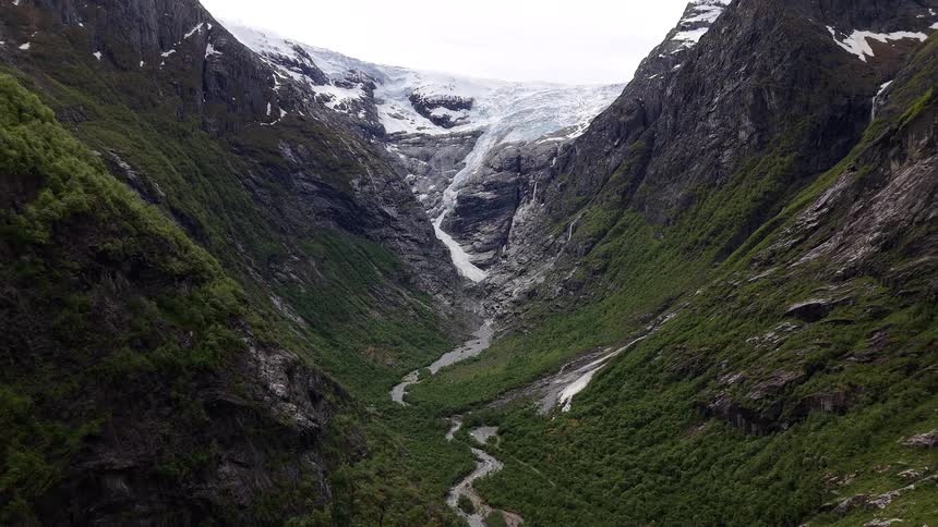 An epic aerial view captures the vast Bondhusbreen glacier in Norway, with a river of meltwater carving its way through a lush green mountain valley