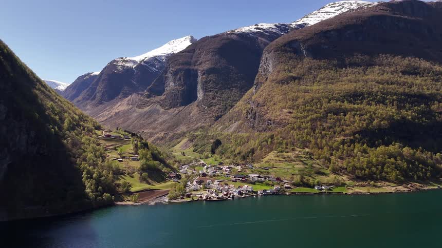 Stunning aerial view of a remote village nestled in a valley on the edge of a Norwegian fjord, with snow-capped mountains towering above