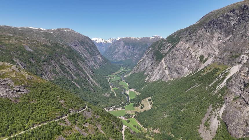 A breathtaking aerial view slowly pulls back to reveal a vast, lush green mountain valley in Norway with snow-capped peaks in the distance
