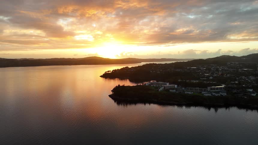 Breathtaking aerial view of a golden sunset reflecting on a tranquil bay with a silhouetted coastal town
