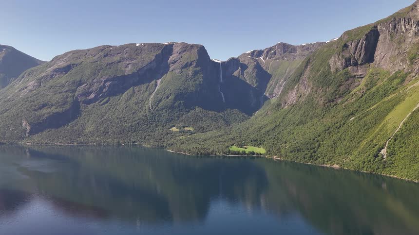 The majestic Mardalsfossen waterfall cascades down the lush green mountainside into the calm waters of Eikesdalsvatnet lake in Norway