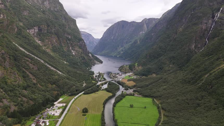 A stunning wide-angle aerial shot of a Norwegian fjord with a river winding through a lush green valley towards the water