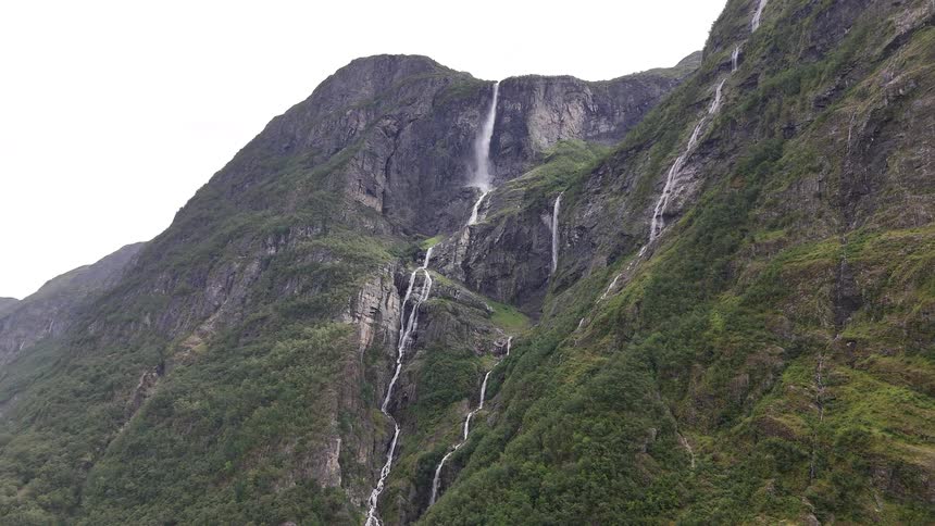 Majestic waterfalls cascade down the steep, lush green slopes of a mountain in the Norwegian fjords