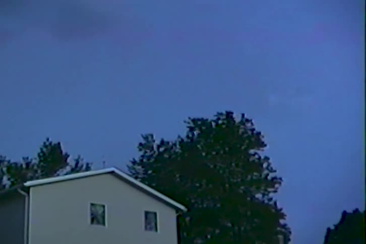Archival footage captures an intense lightning storm illuminating the dark sky over a residential house at night