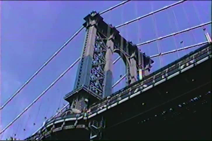 A vintage low-angle shot captures the iconic steel tower of the Manhattan Bridge against a clear blue sky in New York City