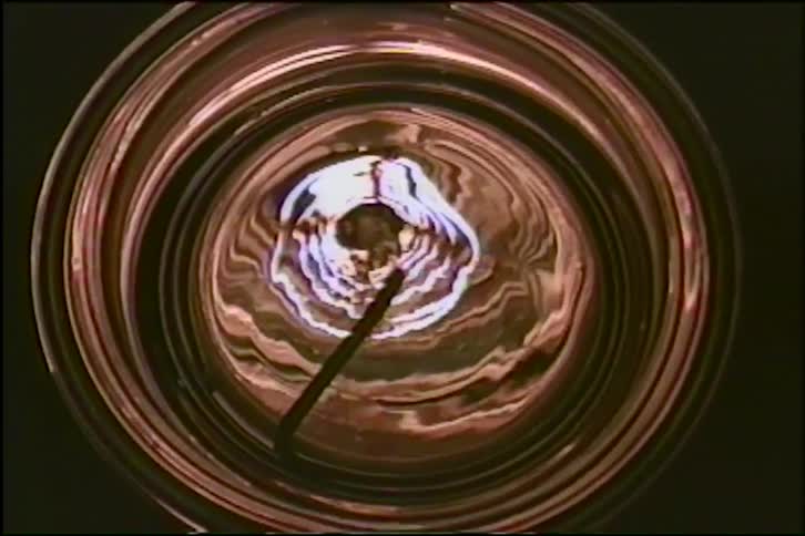 Mesmerizing top-down shot of a swirling, iridescent chemical reaction creating abstract patterns inside a glass beaker as the camera zooms out