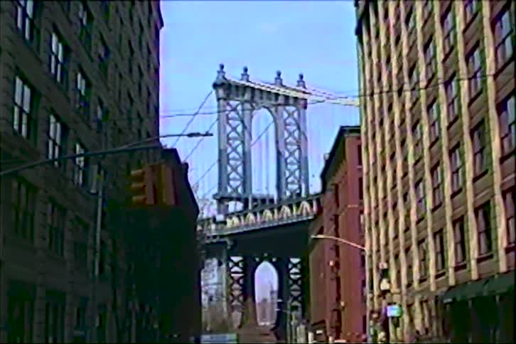 Iconic view of the Manhattan Bridge framed by DUMBO's historic brick buildings on a sunny day, captured on vintage VHS