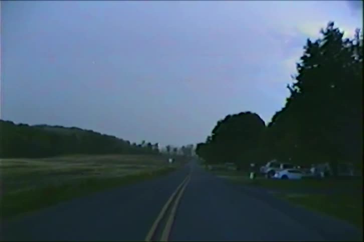 A low-angle point-of-view shot reveals a quiet country road at dusk, following the double yellow lines