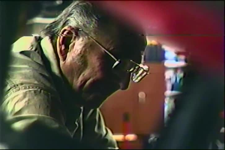 A close-up shot of an elderly craftsman wearing glasses, deeply focused on his work in a home workshop