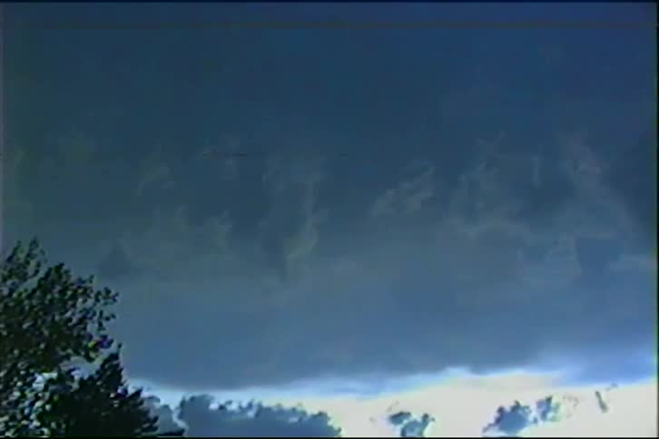 An ominous, dark blue sky is illuminated by flashes of sheet lightning during a severe thunderstorm, captured on vintage footage