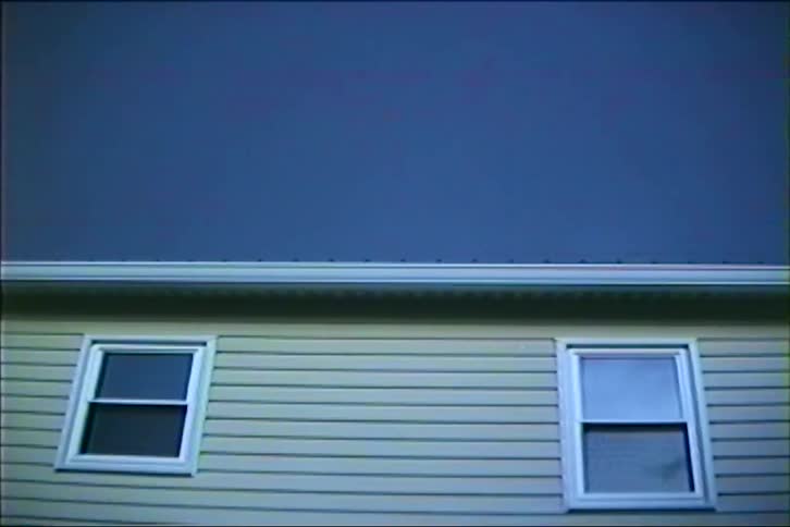 Vintage footage captures a lightning bolt striking across a dark, stormy sky above a suburban house